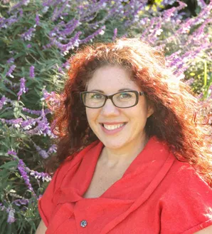 Photo of Amanda Lieber in an orange shirt standing in front of purple flowers.